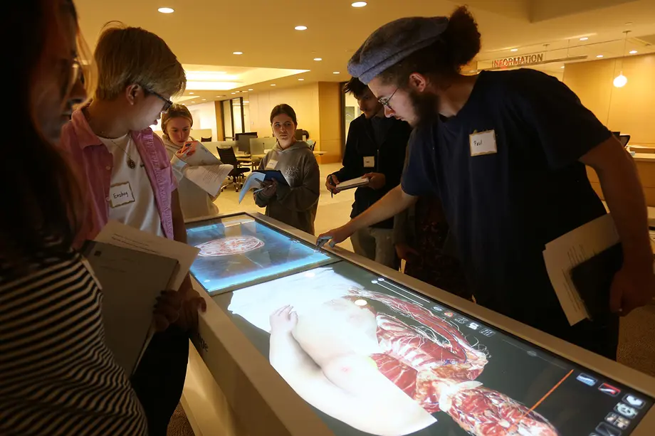 Students stand around a computer table showing a human body with part of the skin removed.