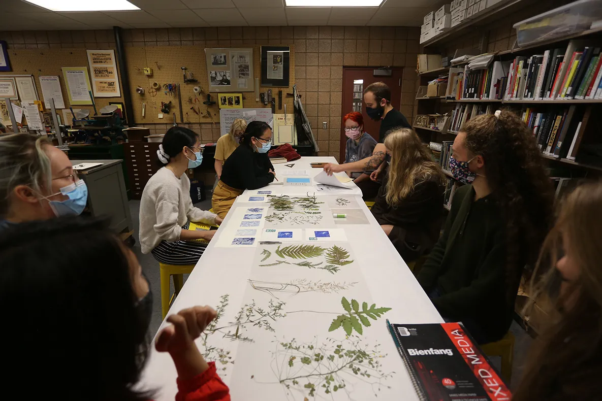 Students sit around a long rectangular table with pressed plants.