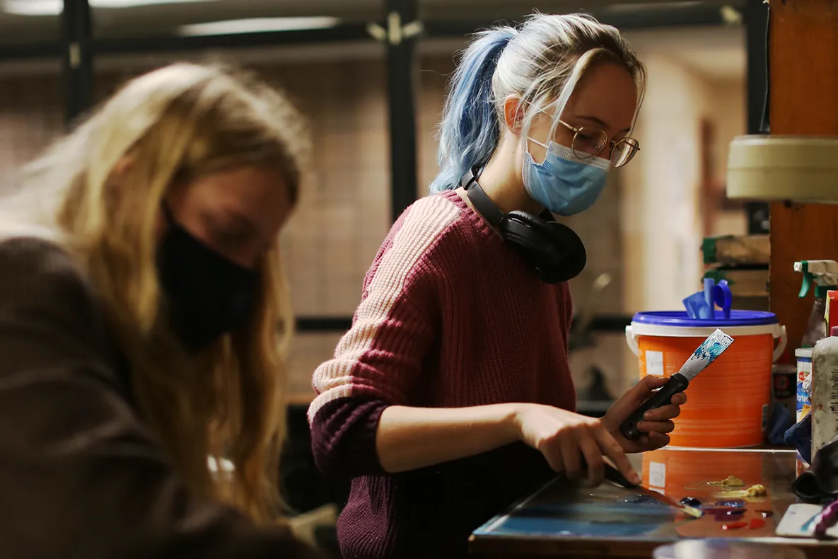 Student using a putty knife to mix paints.