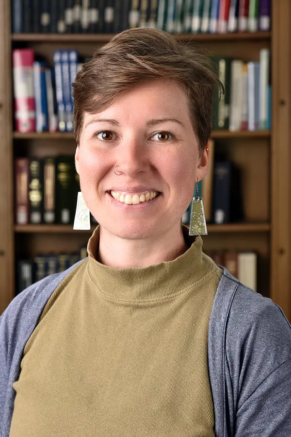 smiling woman with short, brown hair seated in front of a bookshelf