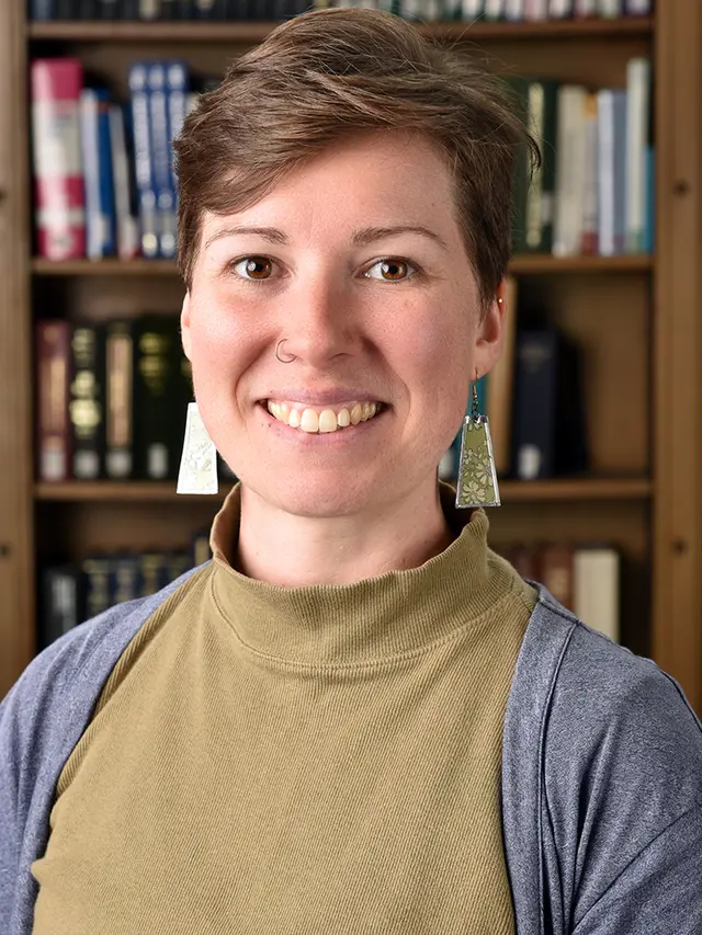smiling woman with short, brown hair seated in front of a bookshelf