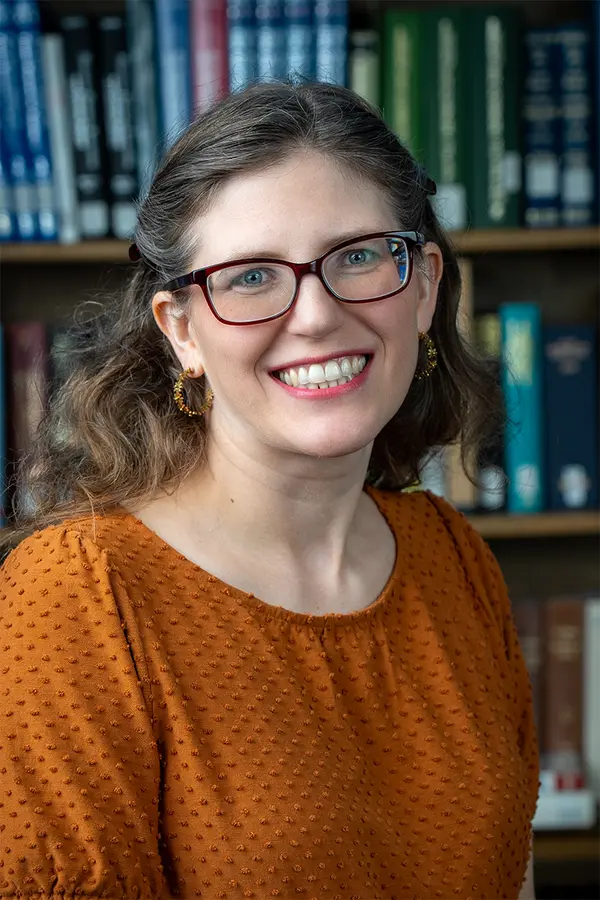 Photograph of Juli McLoone, a white woman with brown hair and glasses, wearing oranged blue eyes, wearing purple.