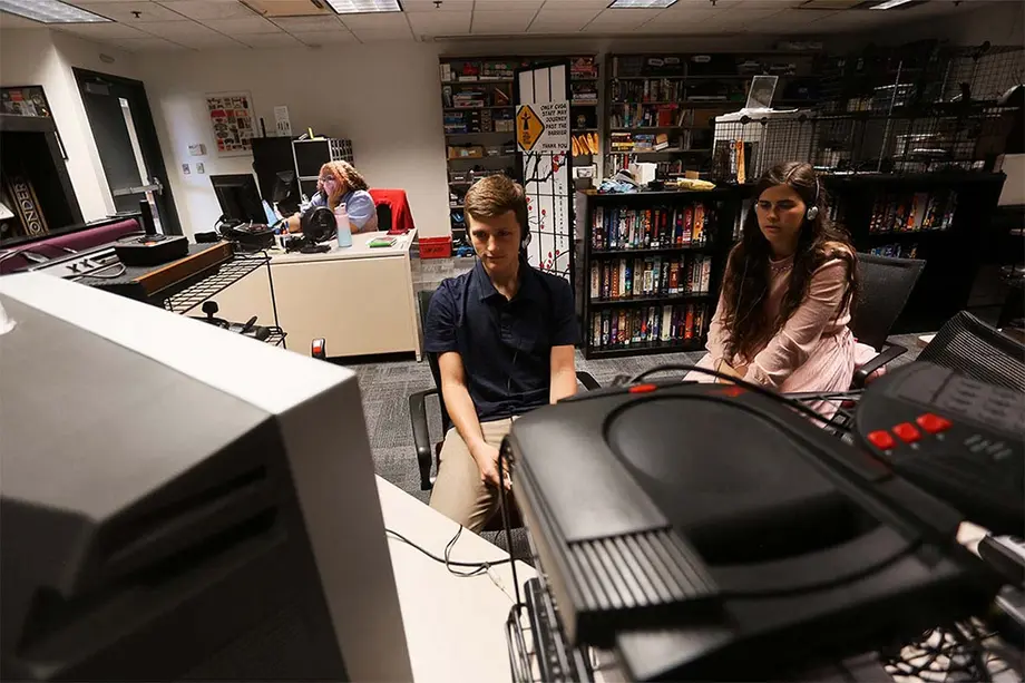 Students playing a video game at a computer the Computer and Video Game Archive with shelves of games in the background.