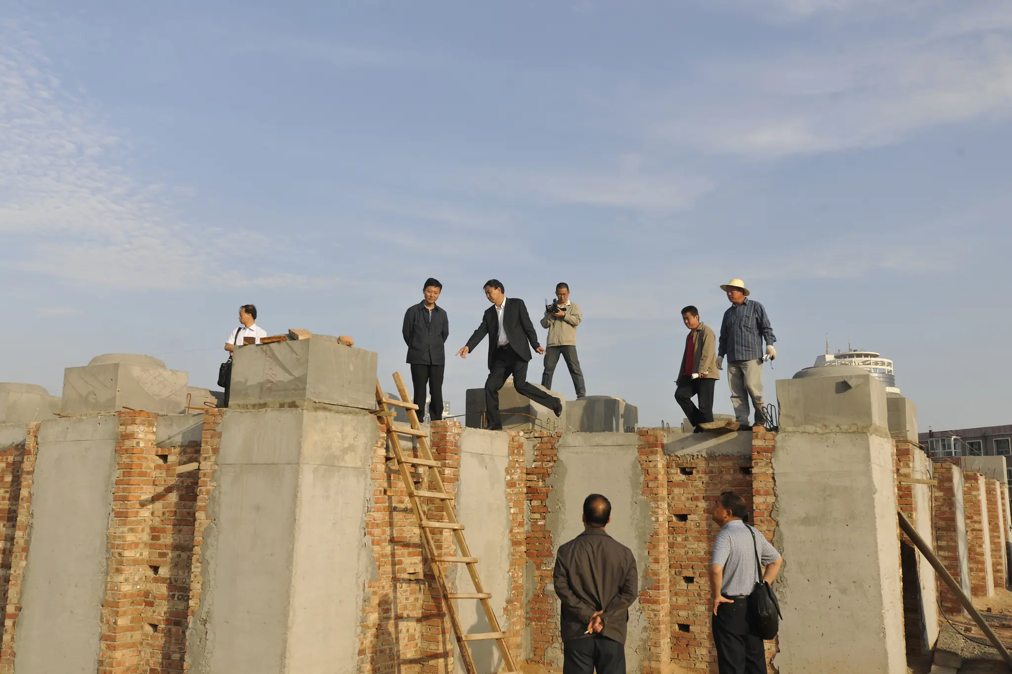 Men standing on top of a cement and brick building, with a ladder leaning from the lower level to the top.