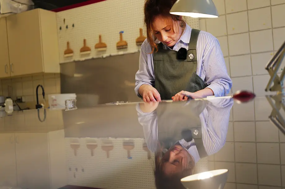 Woman wearing a green apron doing intricate work at a reflective table.