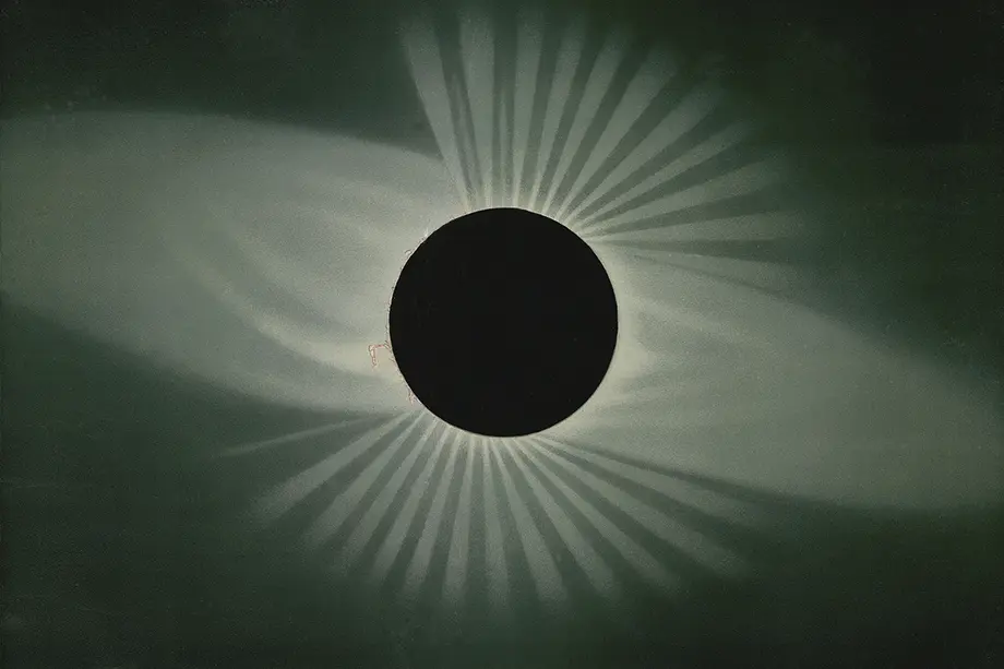 Black circle moon with rays of sun shining out from behind it.