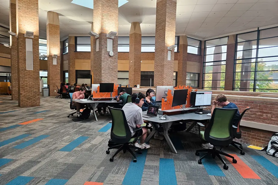 Students working individually at a set of tables with external monitors and short privacy dividers..