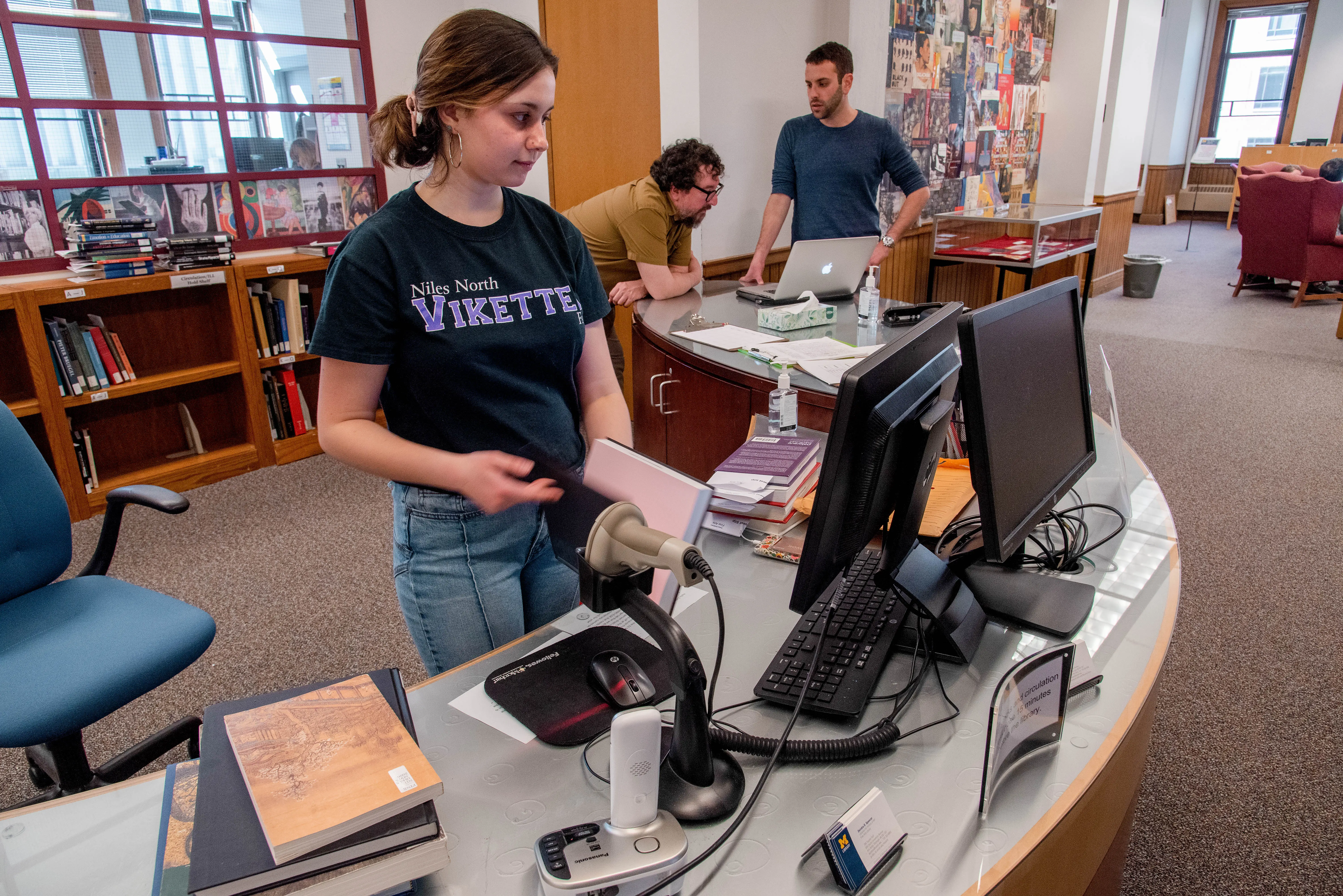 Student staff standing behind the Fine Arts Library Information Services Desk looking at a computer.