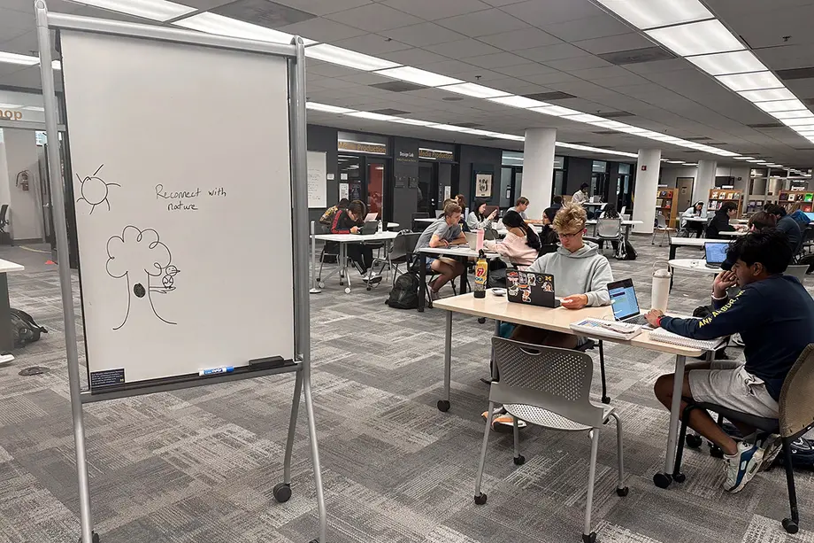 A movable whiteboard and students working at tables on a big open floor. 