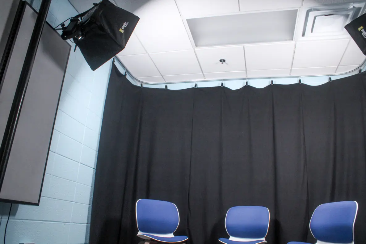 Three chairs in front of a black curtain black backdrop with video lighting.