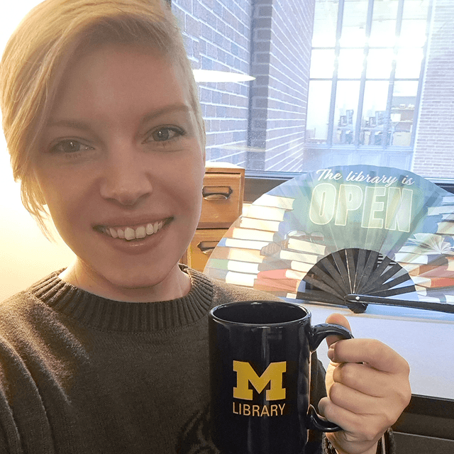 Photo of librarian Beth Havas, smiling and holding a University of Michigan Library mug.