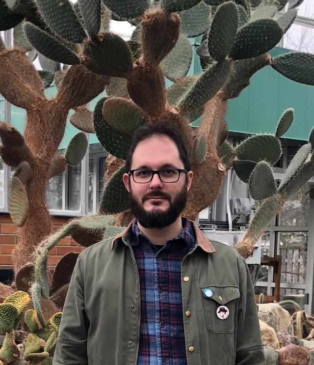 Photograph of Scott Witmer, a bearded white man idling before a large cactus