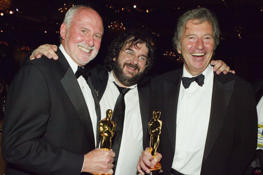 three men in black suits smiling and posing with two oscars