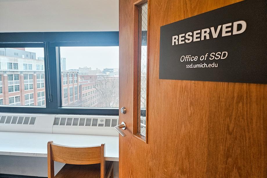 Door with Reserved - Office of SSD sign ajar into a room with a chair, desk, and windows with a view of campus.