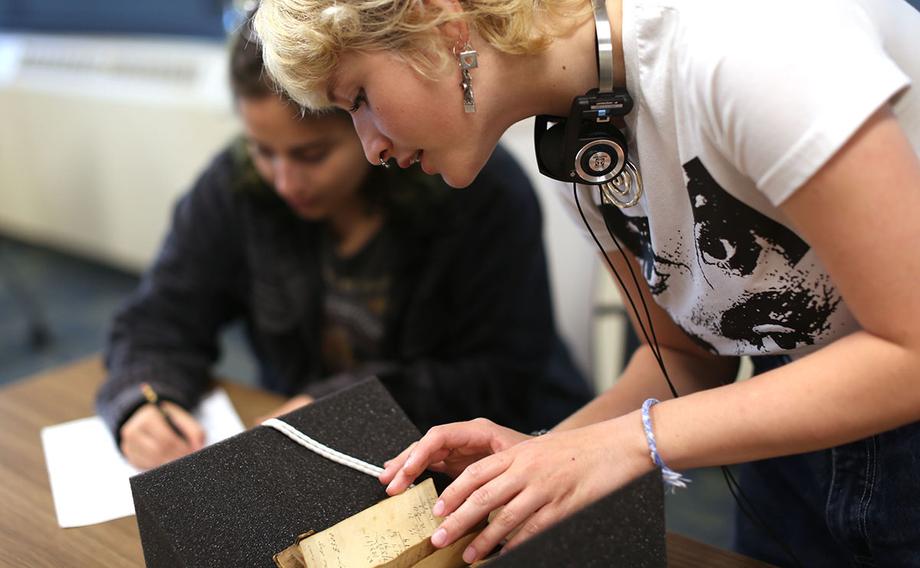 A student leafs through a small, handwritten recipe book that's resting on a foam support.