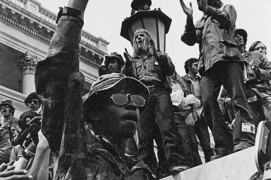 Black and white photo of a project with a Black man wearing sunglasses in center, holding his fist in the air.