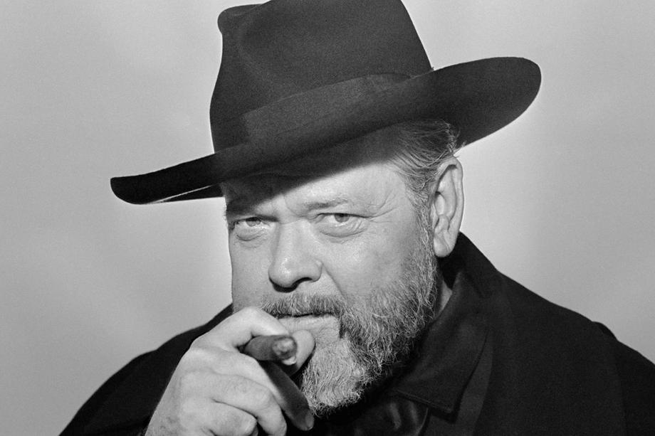 headshot of a man in a black hat holding a cigar