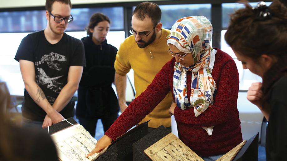 Students gather around an open book of Islamic script.