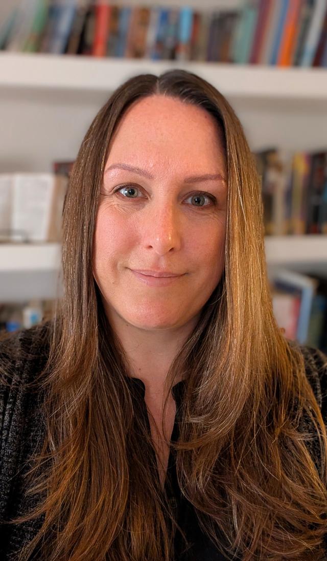 Photo of a white woman with long brown hair in front of a bookshelf