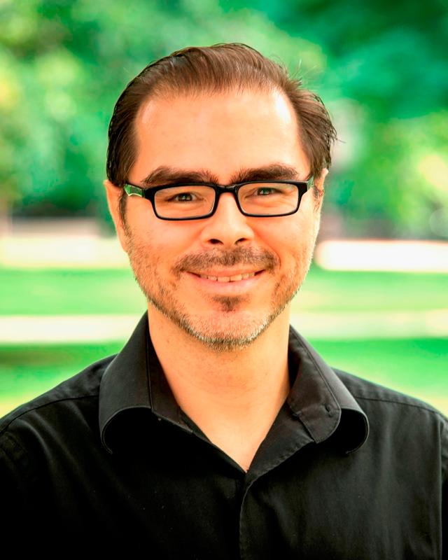 Photograph of Gabriel Duque, a Latino man wearing glasses and a black shirt. 