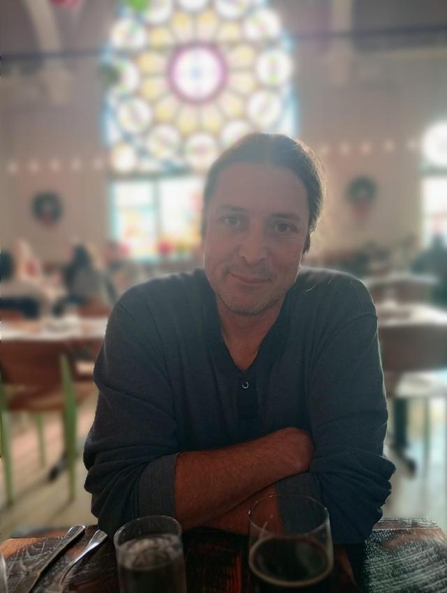 middle aged person seated at table with stained glass window in background