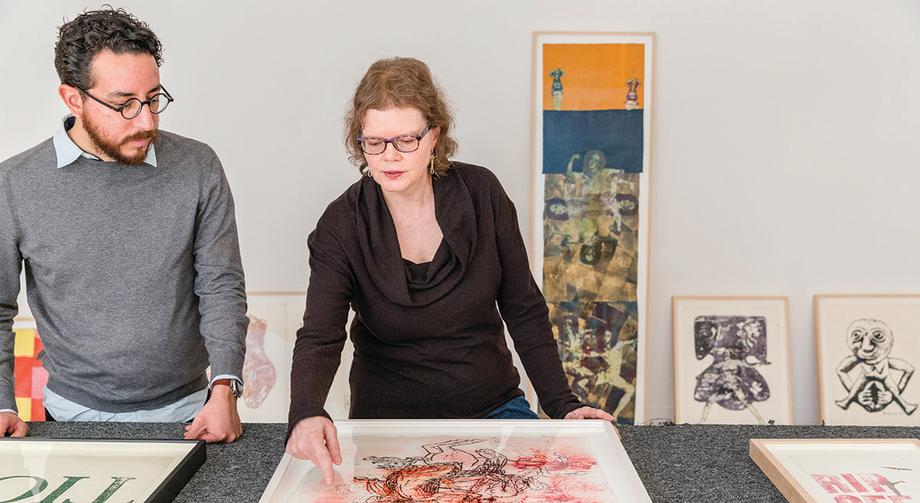 Woman gesturing to at a framed art piece to a man standing next to her.