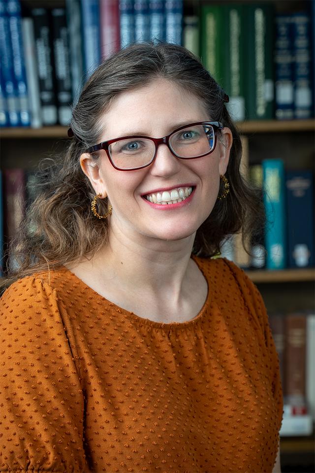 Photograph of Juli McLoone, a white woman with brown hair and glasses, wearing oranged blue eyes, wearing purple.