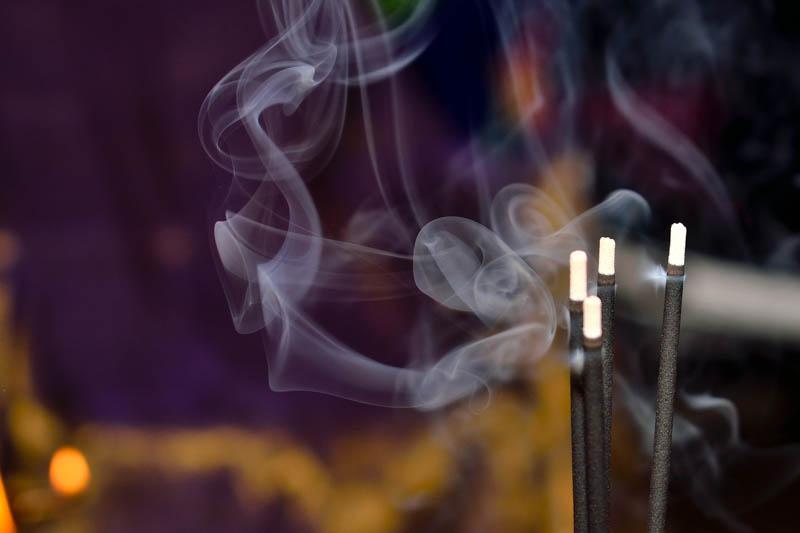 Sticks of incense burning with visible smoke on a dark background.