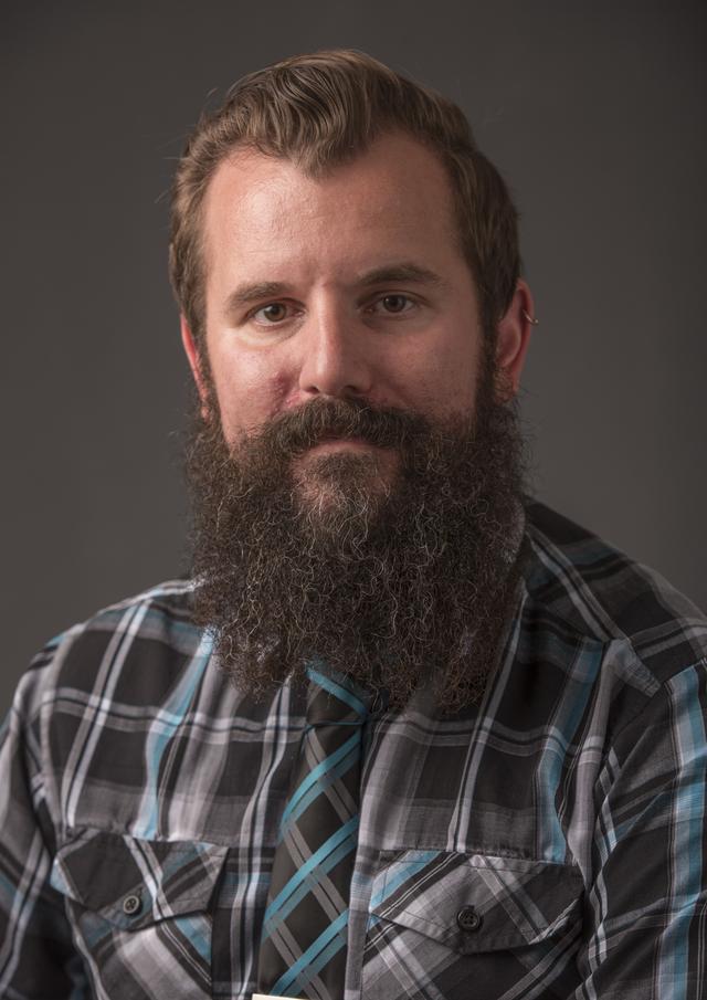 photograph of Stephen Griffes, a man with short brown hair and medium-length beard, wearing a plaid shirt, necktie, and a smile. 