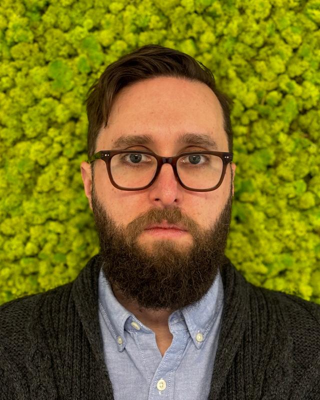 Photo of a bearded man standing in front of a mossy background