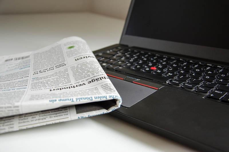 Folded newspaper laying on top of an open laptop.