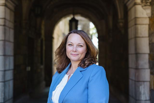 The picture is located near an archway to the Law Quadrangle at the University of Michigan&#039;s Ann Arbor campus. I am a white female with shoulder-length light brown hair, and I have blue eyes. I am wearing a light blue suit jacket with a white shirt underneath.