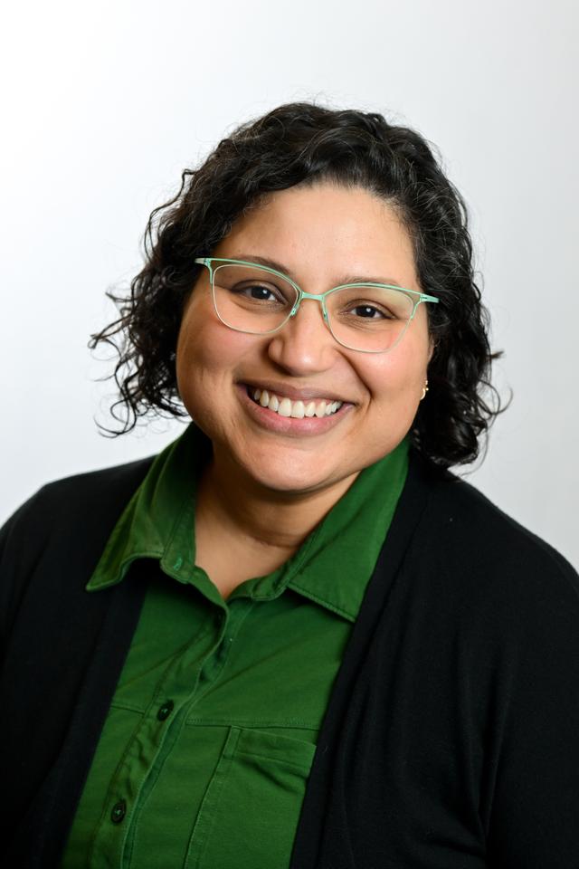 Photograph of Vitalina Robinson, a mixed-race latine woman with light brown skin, wearing glasses, a green dress, and smiling.