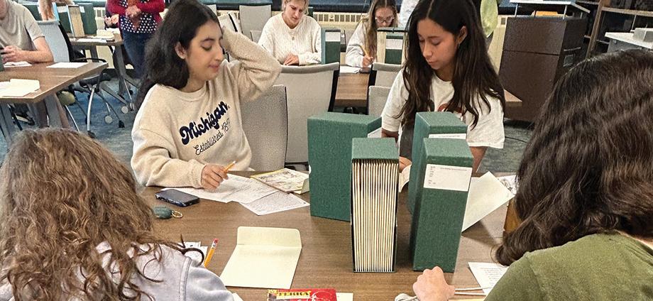 Students working at a table with four green journal boxes.